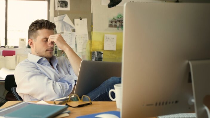 Ein Mann sitzt am Schreibtisch vor einem Monitor in einem Büro ärgert sich über einen erfolgreichen Hackerangriff auf sein Unternehmen  