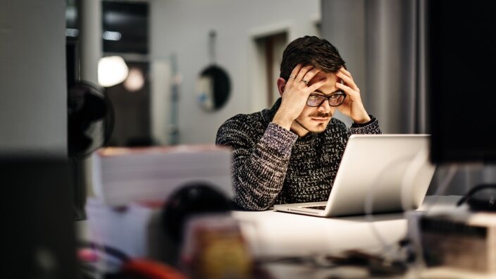 Ein Mann sitzt im Büro vor einem Laptop und grübelt über einen erfolgreichen Cyberangriff auf seinen Arbeitgeber nach.