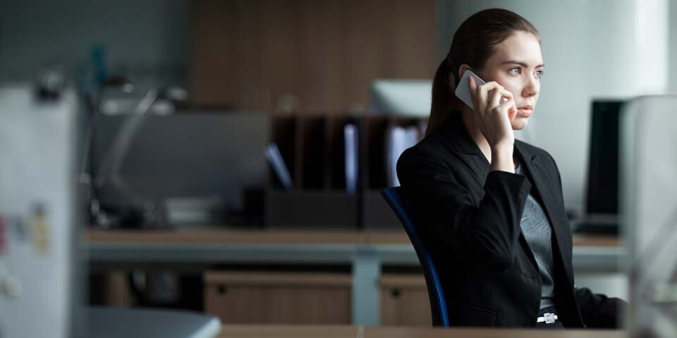 Eine Frau mit Handy am Ohr vorm Rechner, die besorgt aus dem Fenster guckt