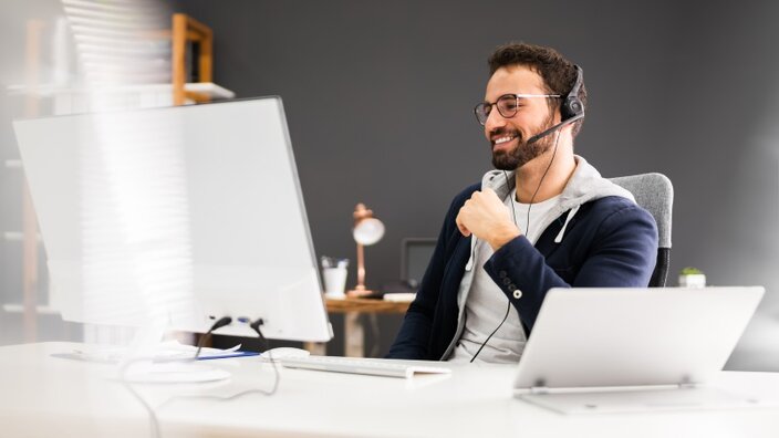 Ein junger Mann mit dunklen Haaren und dunkelblauer Jacke sitzt vor dem Computer und nimmt an einem EWE business Webinar teil.