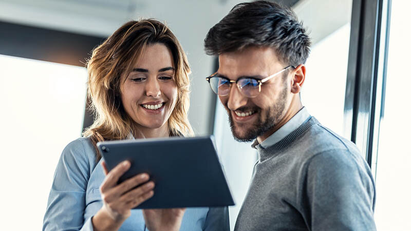 Eine Frau und ein Mann gucken begeistert auf ein Tablet.