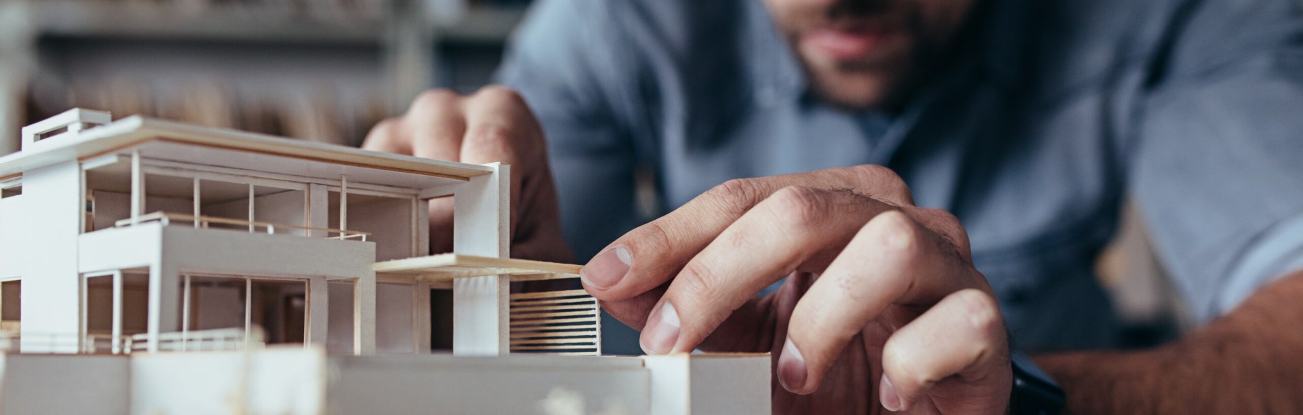 Ein Mann im blauen Hemd setzt vorsichtig Teile in einem Architekturmodell ein.