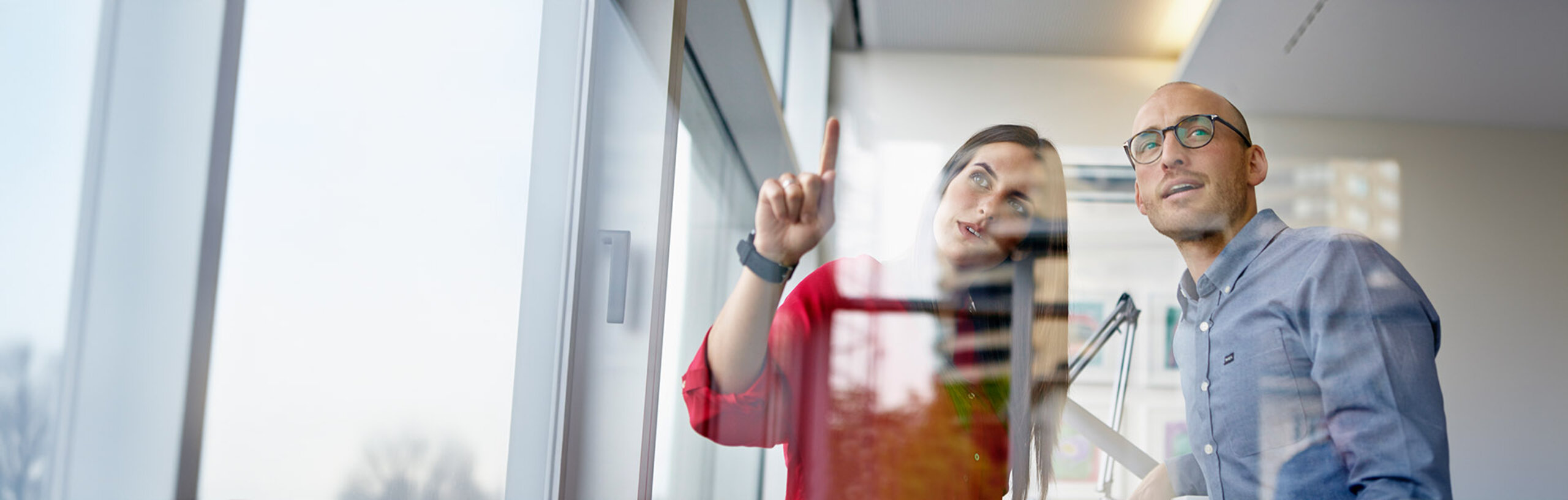 Ein Mann und eine Frau betrachten einen Lösungsansatz in einem Büro, die Frau zeigt auf etwas in der Luft.