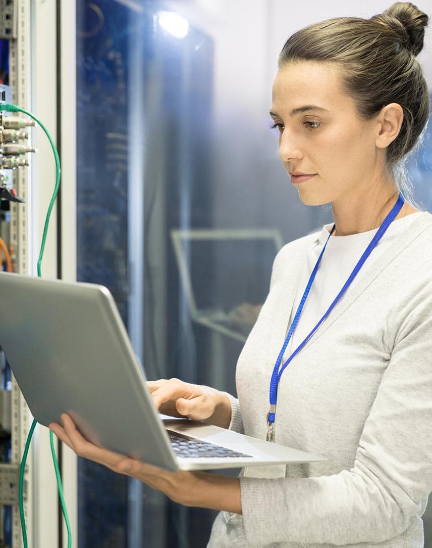 Eine Frau arbeitet mit Laptop an einem Serverschrank.