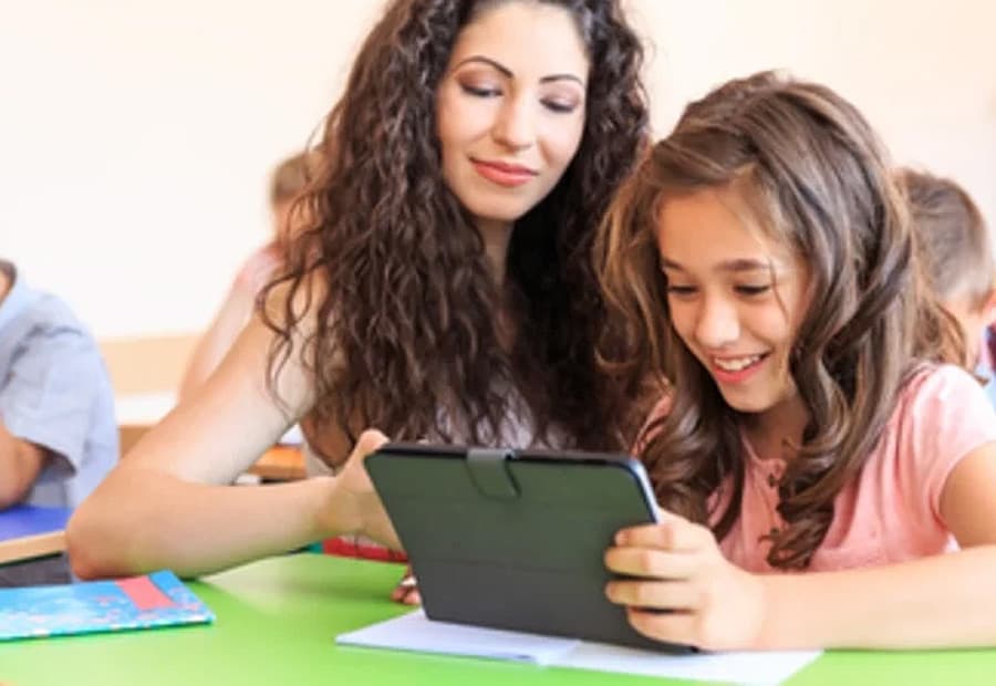 Lehrerin schaut gemeinsam mit einer Schülerin auf ein Laptop