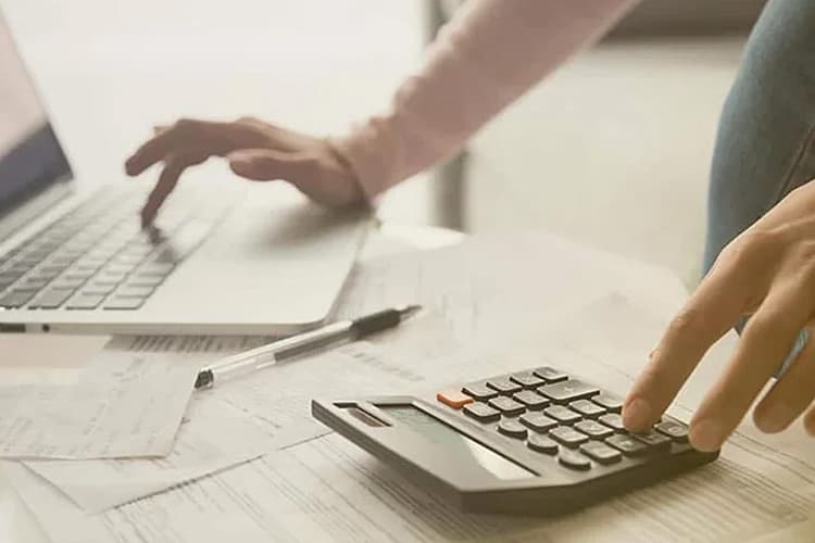 Eine Hand tippt am Laptop, eine Hand auf einem Taschenrechner
