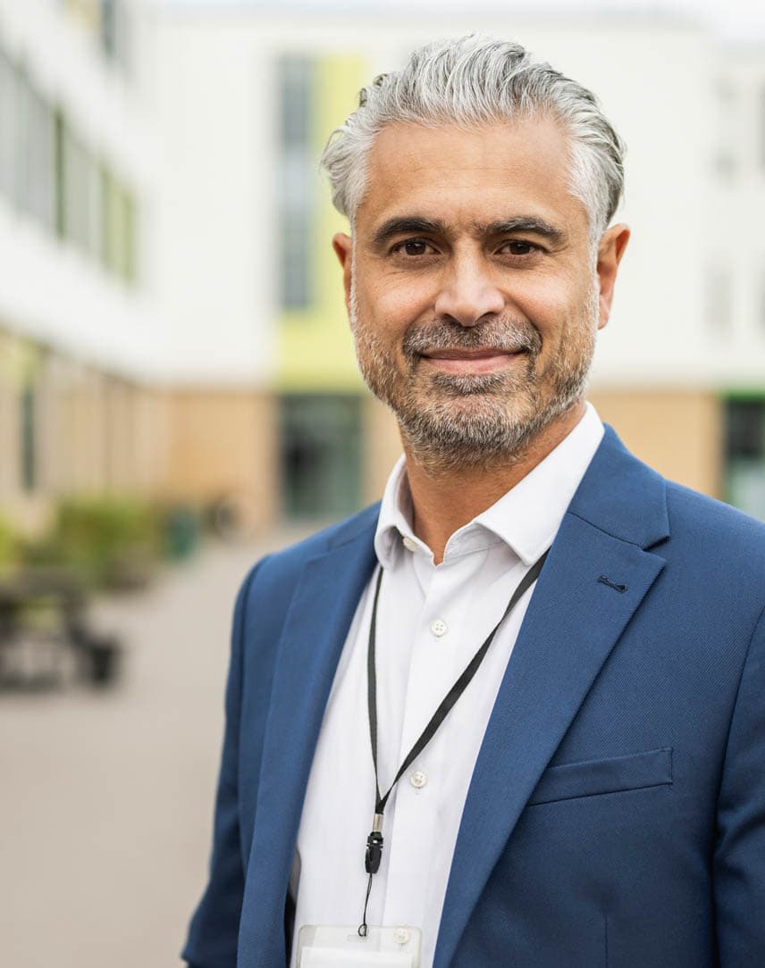 Ein Mann im blauen Jacket steht vor einem größeren Gebäudekomplex.