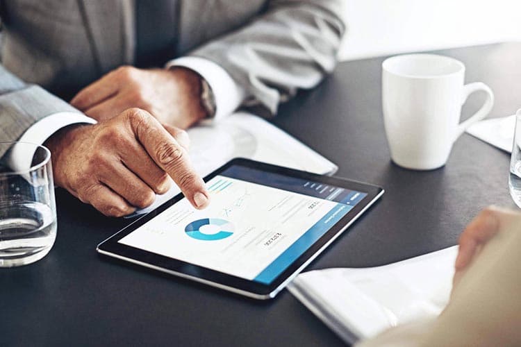Ein Tablet mit Diagramm auf einem Tisch, auf das eine Person zeigt