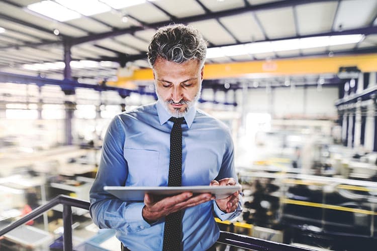 Ein Mann in Business-Kleidung in einer Halle, der etwas auf einem Tablet ansieht