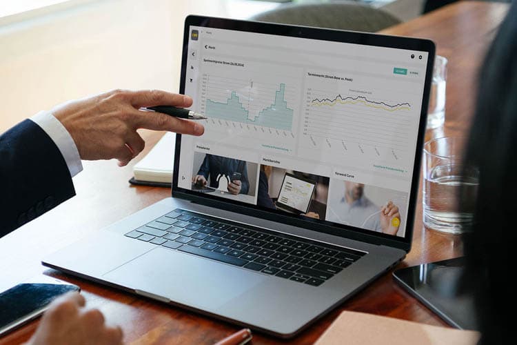 Eine Person deutet auf Diagramme im Business Portal, das auf einem Laptop angezeigt wird.
