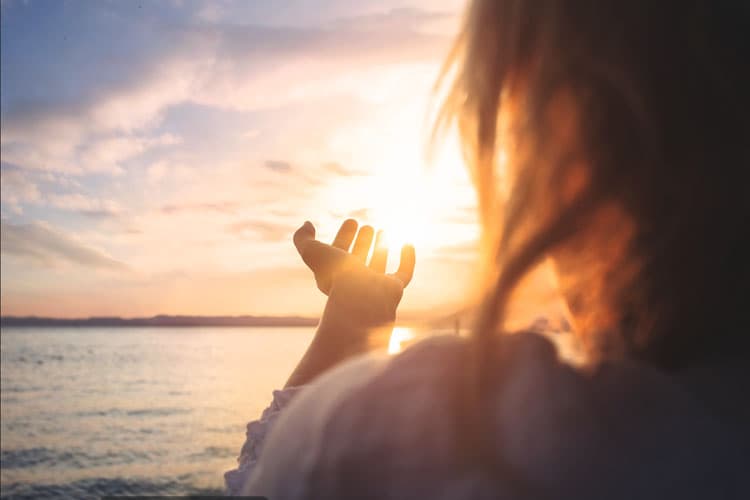 Eine Frau an einem Strand, die ihre Hand in Richtung Sonne ausstreckt