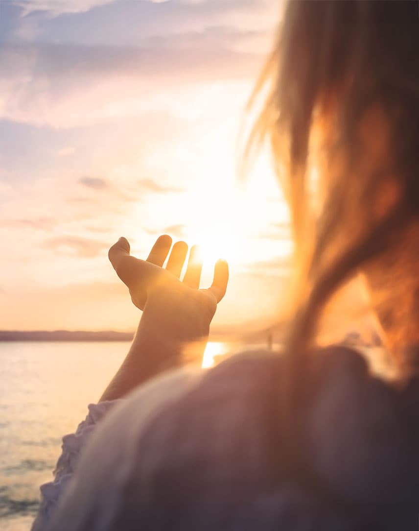 Eine Frau an einem Strand, die ihre Hand in Richtung Sonne ausstreckt