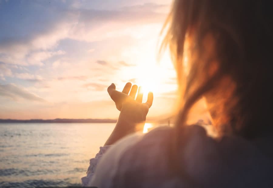 Eine Frau an einem Strand, die ihre Hand in Richtung Sonne ausstreckt