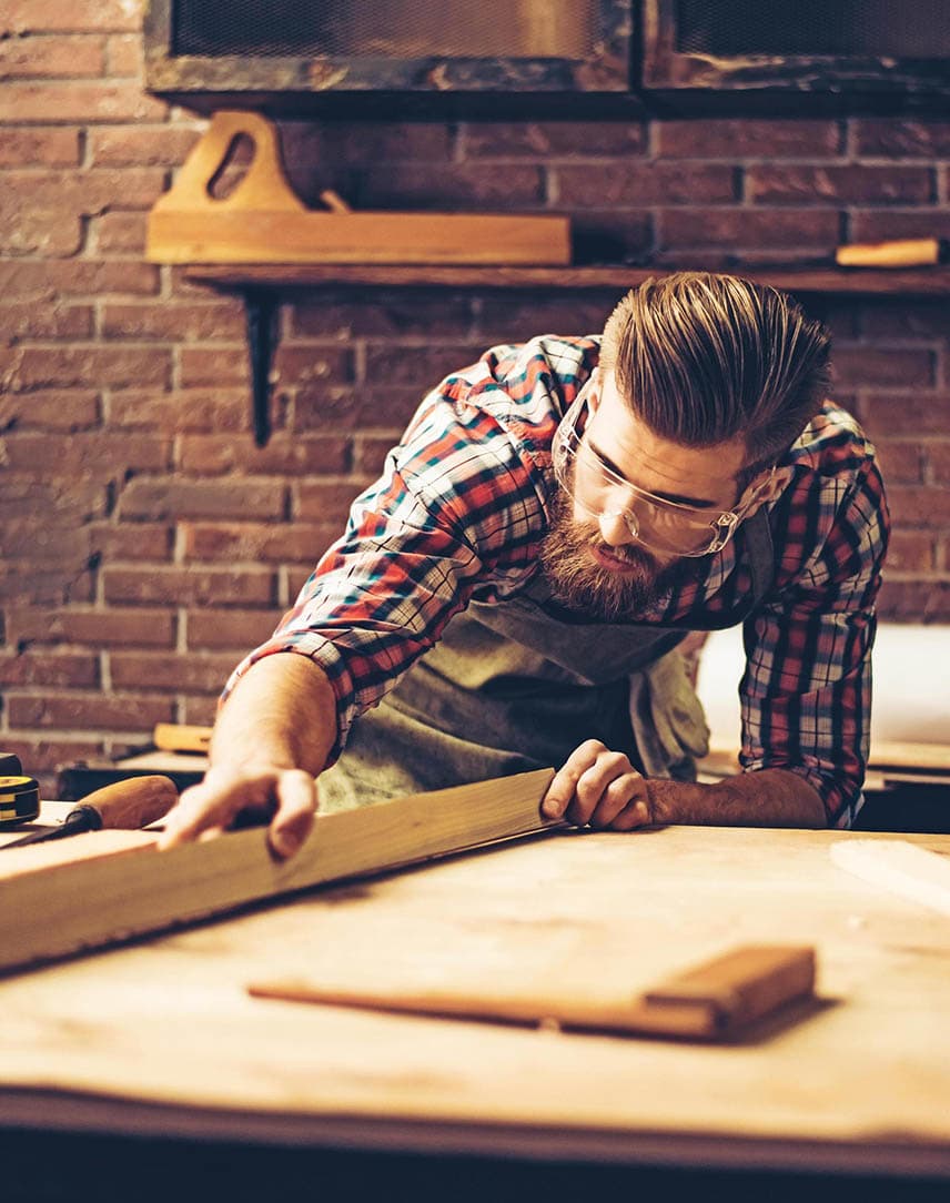 Ein Tischler im karierten Hemd bei der Arbeit an seiner Werkbank
