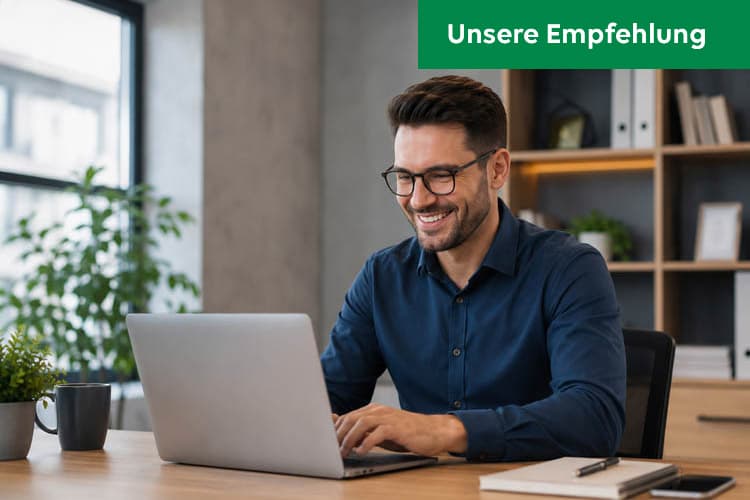 Ein Mann im dunkelblauen Hemd sitzt an einem Schreibtisch und bedient ein Laptop.