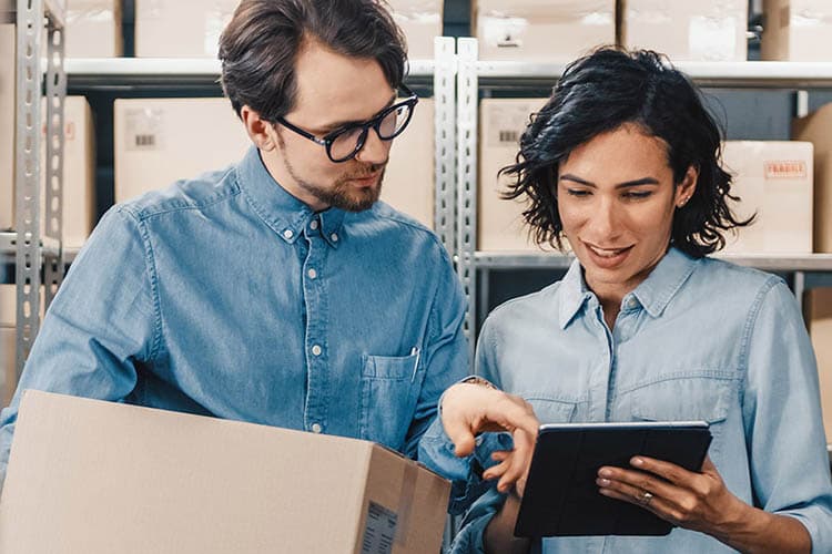 Eine Frau und ein Mann in einem Lagerraum, die etwas auf einem Tablet prüfen