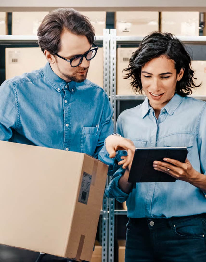 Eine Frau und ein Mann in einem Lagerraum, die etwas auf einem Tablet prüfen