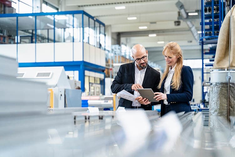 Ein Mann und eine Frau besprechen etwas an einem Tablet in einer Produktionshalle.