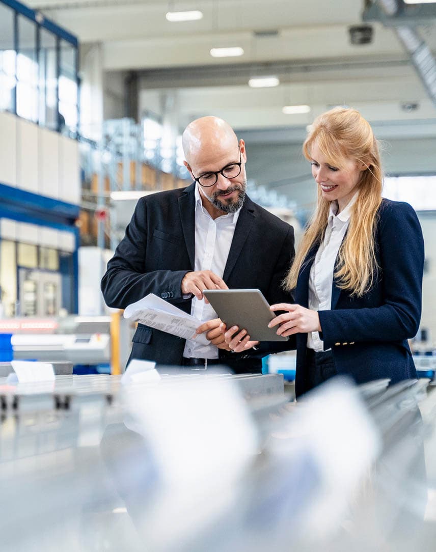 Ein Mann und eine Frau besprechen etwas an einem Tablet in einer Produktionshalle.