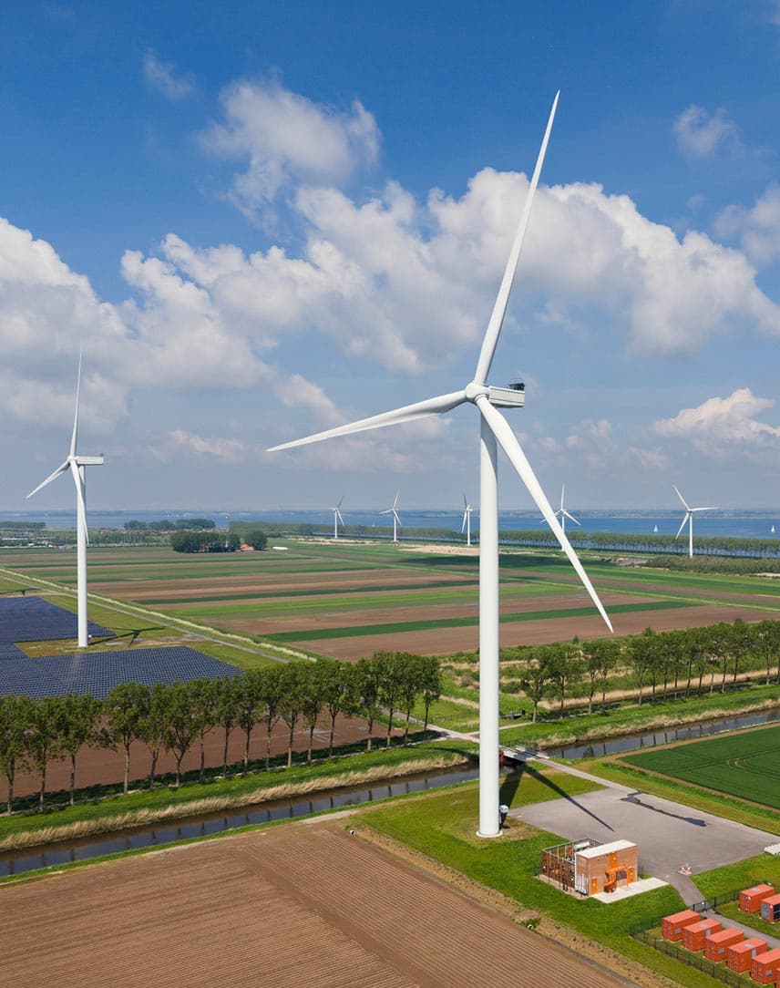 Windkraft- und PV-Anlagen auf einer Freifläche, davor ein Batteriespeicher