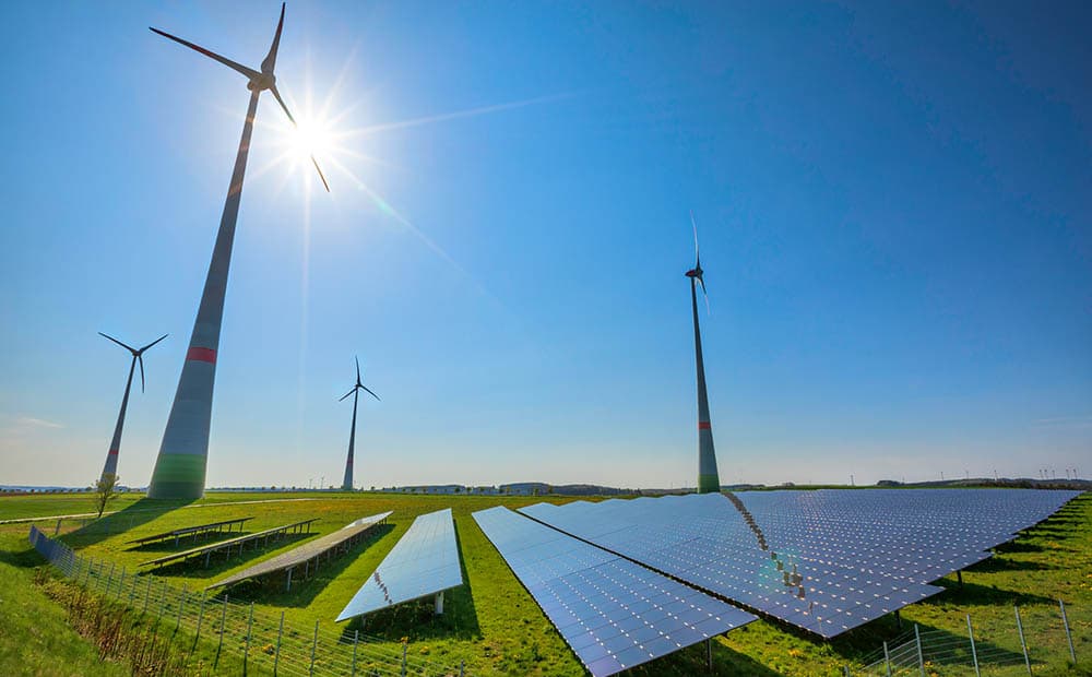 Eine PV-Freiflächen-Anlage, dahinter Windräder