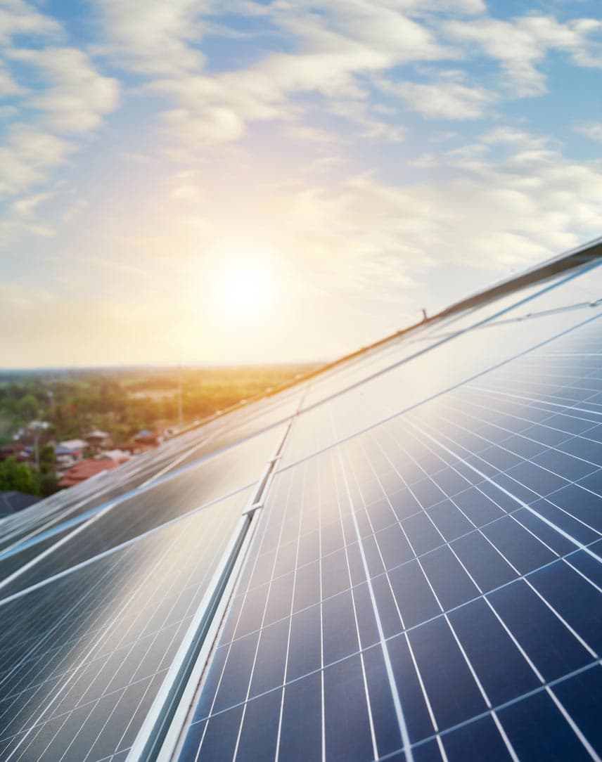 PV-Module auf einem Hausdach, das von der Sonne beschienen wird, im Hintergrund Landschaft mit Häusern