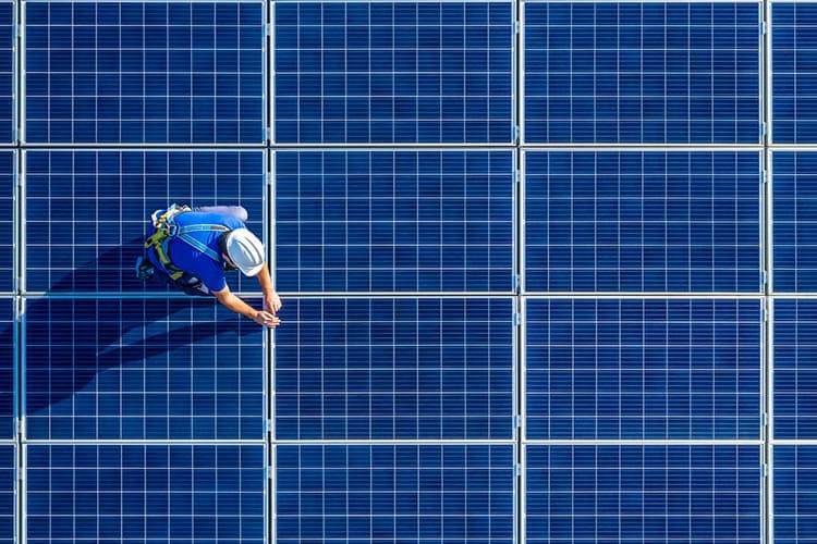 Ein Techniker mit Helm, der auf einer PV-Fläche kniet