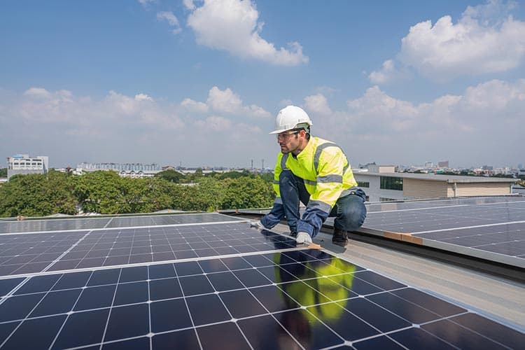 Ein Techniker in gelber Warnweste arbeitet an PV-Modulen auf einem Dach.