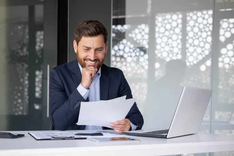 Ein Mann mit Sakko, der Unterlagen ansieht, davor ein Laptop