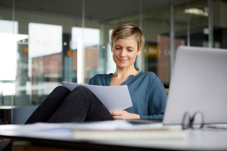 Eine Frau, die Unterlagen ansieht, davor ein Laptop