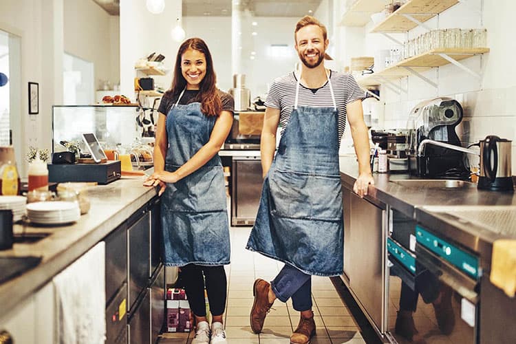 Eine junge Frau und ein junger Mann, die als Baristas in der Küche eines Cafés stehen.