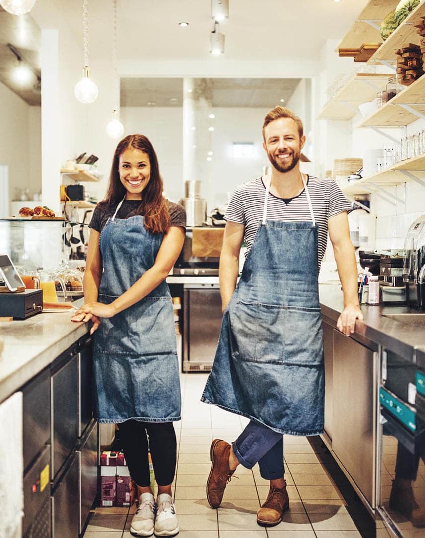 Eine junge Frau und ein junger Mann, die als Baristas in der Küche eines Cafés stehen.