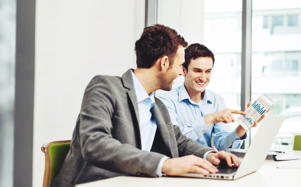 Zwei Männer an einem Arbeitsplatz mit einem Laptop, die ein Diagramm ansehen
