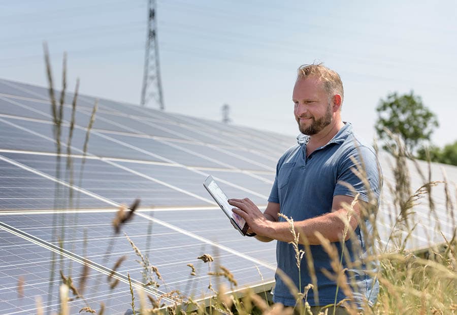 Ein Mann mit Tablet vor einer PV-Freiflächenanlage