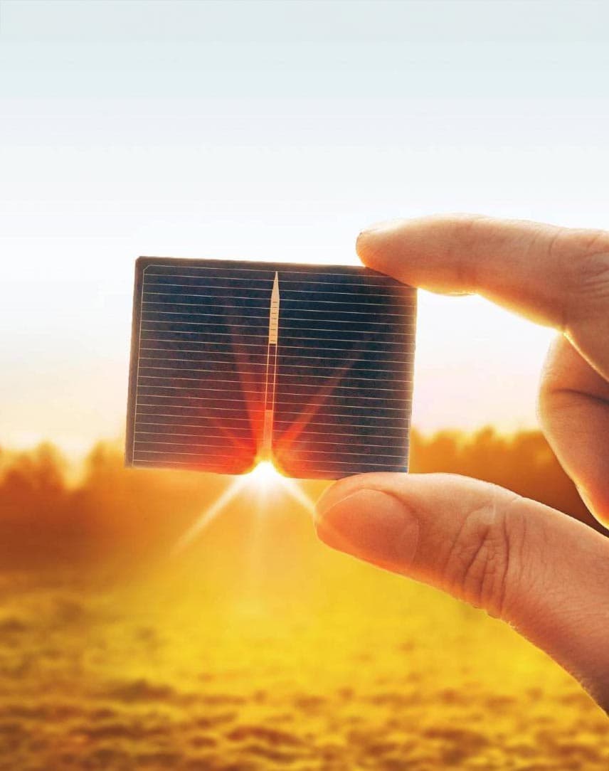 Ein Hand mit PV-Modul vor dem Sonnenuntergang, im Hintergrund eine Wiese