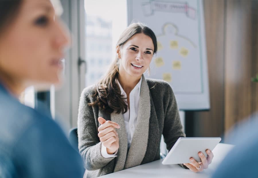 Eine Frau an einem Tisch erklärt KollegInnen etwas mithilfe eines Tablets
