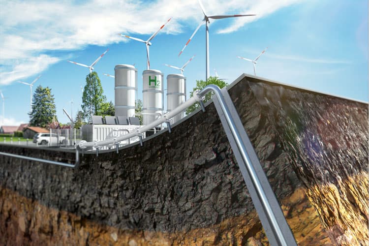 Eine Wasserstoffleitung, die aus dem Erdreich kommt und zu einer Wasserstoffanlage mit Elektrolyseuren führt, im Hintergrund Windräder