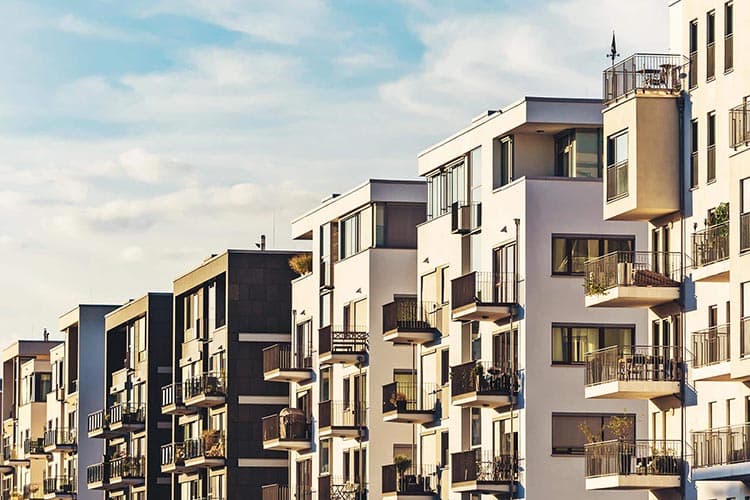 Ein Häuserwand moderner Wohnblocks, dahinter blauer Himmel mit einigen Wolken