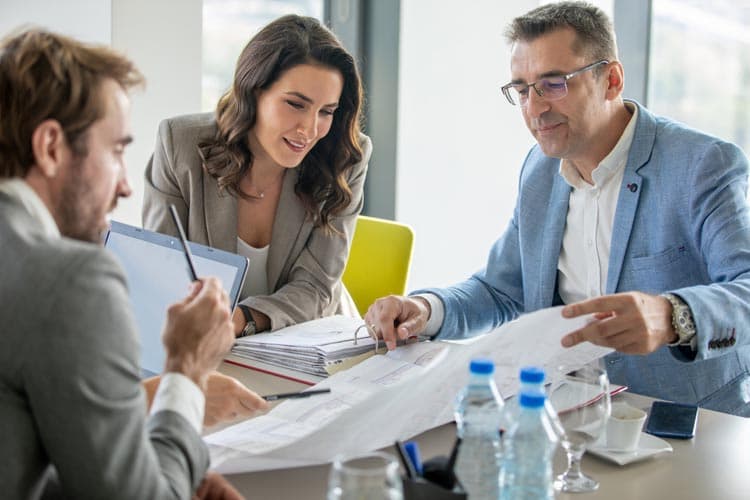 Drei Personen besprechen einen Plan an einem Tisch.