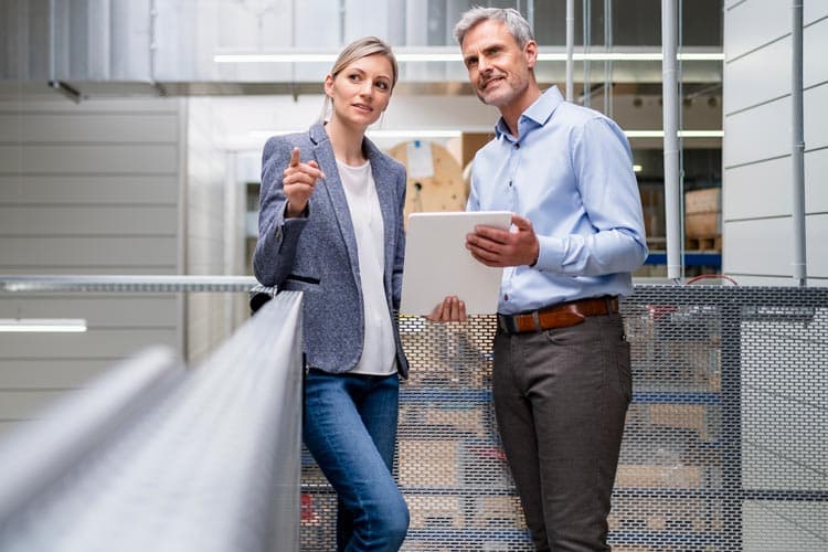 Eine Frau, die auf etwas zeigt, und ein Mann, der ein Tablet hält, besprechen etwas in einer Werkhalle