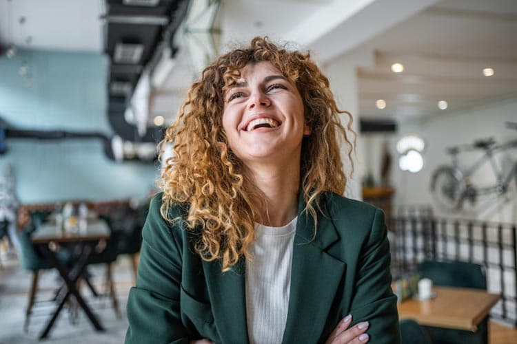 Eine Frau in grünem Oberteil verschränkt die Arme und lacht.