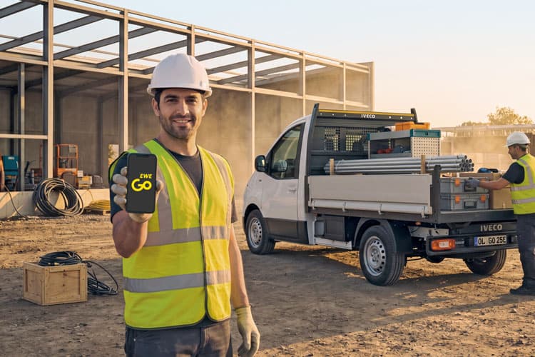 Ein Handwerker mit Warnweste auf einer Baustelle, der eine EWE Go-Ladekarte zeigt