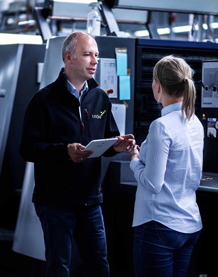 Ein Mitarbeiter von Limon mit einem Tablet in der Hand bespricht etwas mit einer Mitarbeiterin in einer Produktionshalle.