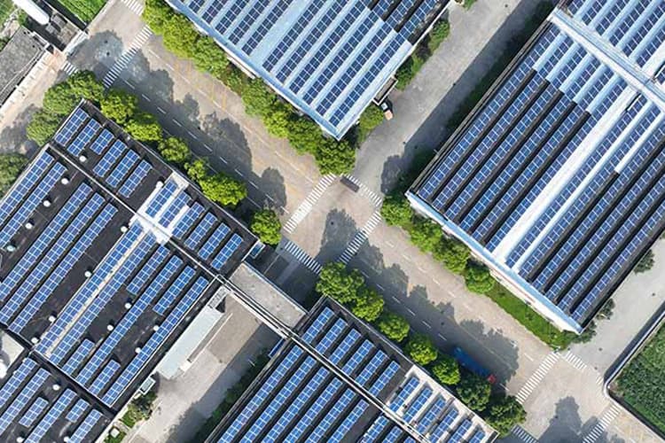 Luftaufnahme von mehreren Gebäuden mit Solarpanelen auf den Dächern und dazwischen verlaufenden Straßen mit Fußgängerüberwegen