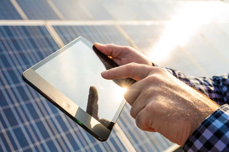 Hand tippt auf Tablet vor Solarpanelen im Sonnenlicht