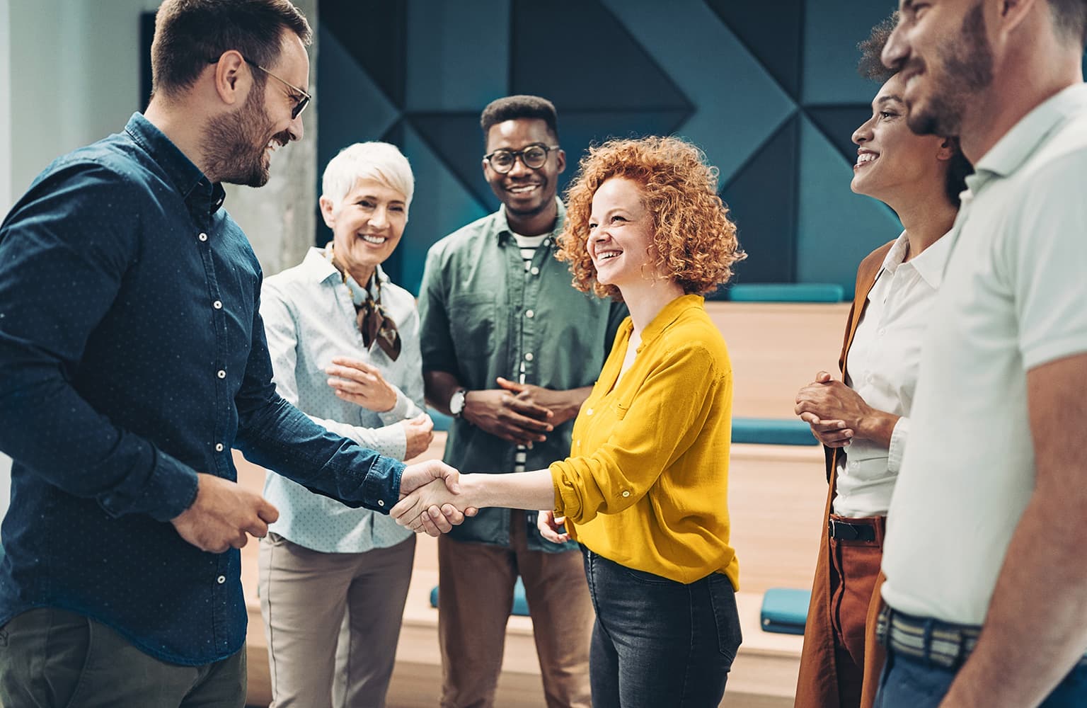 Mehrere Personen stehen in einem Raum, zwei davon geben sich die Hand, während die anderen zuschauen.