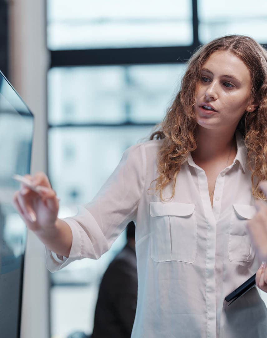 Eine Frau erklärt einer Kollegin etwas an einem großen Bildschirm.