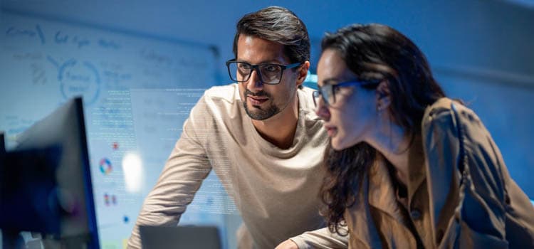 Eine Frau und ein Mann gucken auf ein Bildschirm in einem Büro.