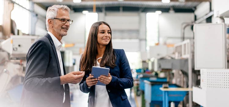 Eine Frau mit Tablet und ein Mann stehen in einer Produktionshalle und besprechen etwas.