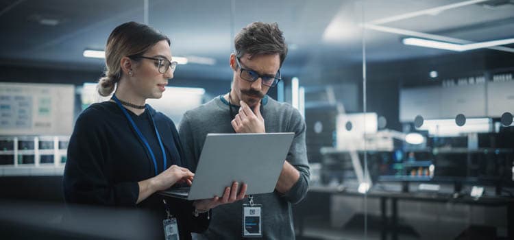 Eine Frau und ein Mann prüfen etwas an einem Laptop in einem Büroraum.